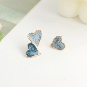 Asymmetric heart stud earrings in blue enamel with gold plating on a clean background