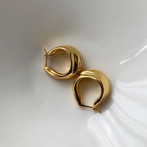 Minimalist chunky golden hoop earrings with high-polish finish on white ceramic plate