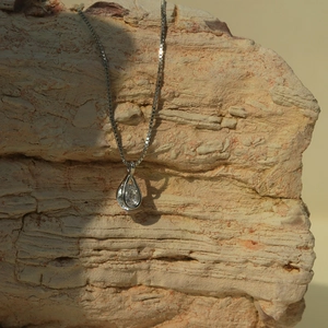 Dettaglio del ciondolo a goccia in cristallo su catena d'argento e sfondo di roccia