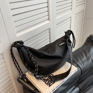Detail of black nylon dumpling bag with woven rope strap and Fashion patch on white books