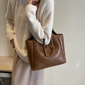 Brown quilted tote bag with chain strap worn by model in an elegant lifestyle setting