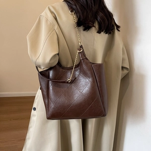 Dark brown large quilt pattern tote bag with gold chain strap worn by a model