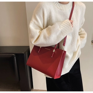 Dettaglio della borsa tote in pelle rossa con scritte dorate su un maglione bianco