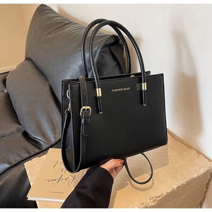 Dettaglio borsa tote in pelle nera opaca con fibbia dorata e tracolla su base in pietra