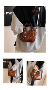 Detail of brown leather bucket bag featuring a cute black cat charm and gold buckle