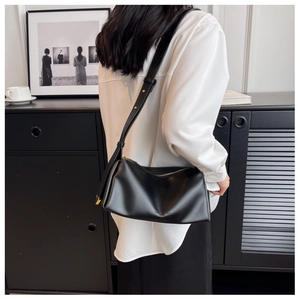 Minimalist black leather underarm bag shown on shoulder in a modern lifestyle setting