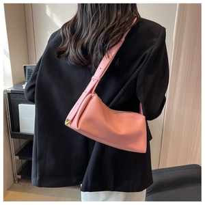 Pink leather baguette bag with heart charm shown on shoulder over a black blazer
