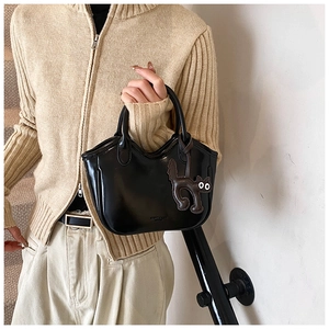 Detail of oil wax leather tote bag featuring a scalloped edge and cute cat charm accessory