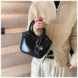 Close-up of shiny black oil wax leather tote bag featuring a cute cat-shaped charm