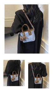 Detail of light blue denim bucket bag with brown leather handles and dog charm accessory