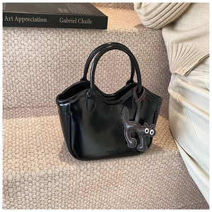 Detail of black glossy leather bucket bag with wave edge and cartoon cat charm