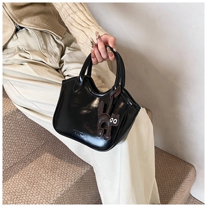 Detail of glossy black oil wax leather tote bag with a cute cat pendant and embossed logo