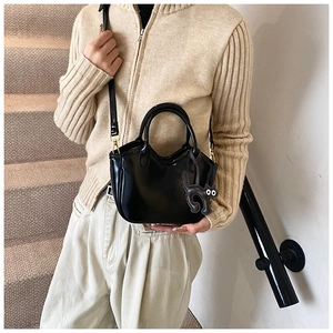 Detail of black glossy leather handbag with cute cat charm held by a model on stairs