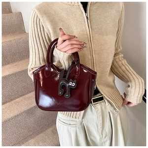 Detail of burgundy wax leather tote with glossy finish and cute cat accessory