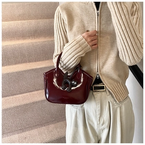 Detail of burgundy wax leather tote bag with cute black cat charm accessory and handle