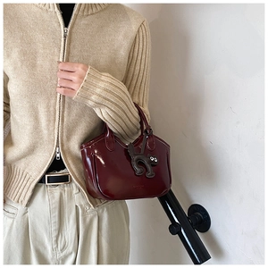 Detail of burgundy wax leather bucket bag with black cat charm held by a model