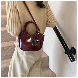 Detail of burgundy glossy leather handbag featuring a cute black cat pendant and strap