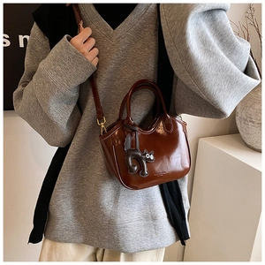 Detail of a brown oil wax leather tote bag with a small black cat charm and shoulder strap