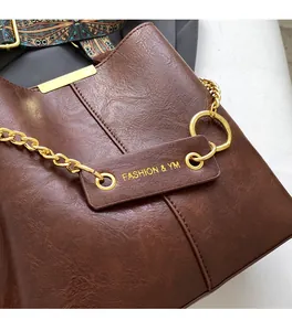 Detailansicht der braunen Lederstruktur mit goldener Kette und Taschenanhänger