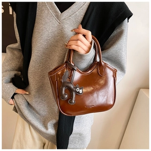 Detail of vintage brown wax leather bucket bag with black cat charm and brand logo