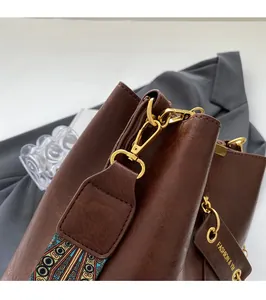 Detail der dunkelbraunen Ledertasche mit goldenen Metallhaken und Ethno-Webgurt