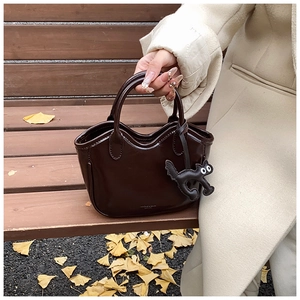Close-up of brown oil wax leather tote with cute cat charm against autumn background