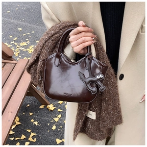 Detail of dark brown oil-wax leather mini tote with a cute cat charm in autumn setting