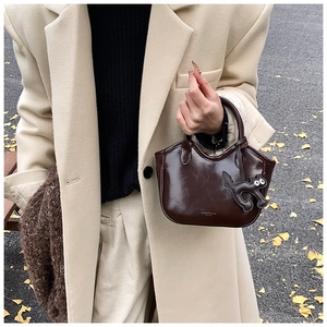 Close-up of brown wax leather tote bag with a cute black cat pendant in an autumn setting
