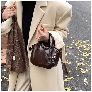Deep brown oil wax leather mini tote bag detail with cute cat charm in autumn outdoor setting