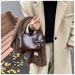 Detail view of dark brown oil wax leather bucket bag with a cute cat charm accessory