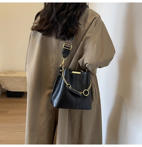 Detail einer glänzenden schwarzen Beuteltasche mit Goldkette und gemustertem Gurt
