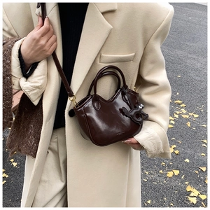 Detail view of glossy oil wax leather tote bag with a cartoon charm in autumn street setting