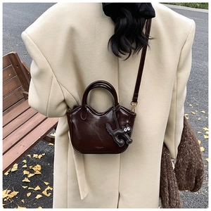 Detail of dark brown oil wax leather tote with cute cat charm in an autumn outdoor setting