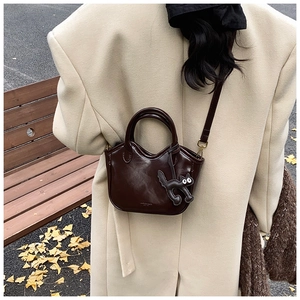 Chocolate brown leather tote bag with a black cat charm shown in an autumn street setting
