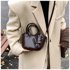 Detail of dark brown leather tote bag with cute cat charm and autumn styling