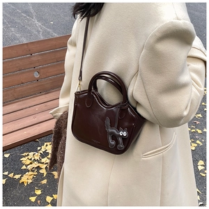 Detail of dark brown wax leather tote bag featuring a cute cat charm on yellow ginkgo leaves
