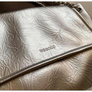 Macro detail of silver wrinkled leather texture and metal chain on the underarm tote bag
