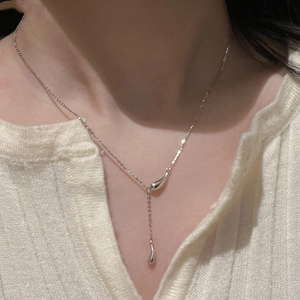 Detail of silver teardrop tassel necklace on woman collarbone over white knit top