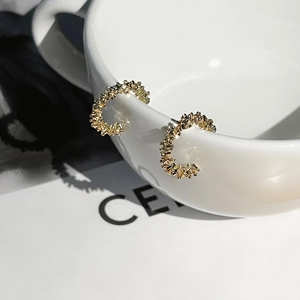 Macro detail of gold C-shaped earrings with irregular lava texture on white ceramic edge