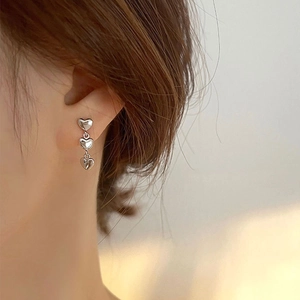 Three linked heart pendant earrings in polished silver metal worn by model