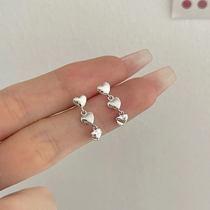 Detail showing triple silver heart drop earrings with a polished metallic finish