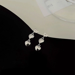 Macro shot of silver triple-heart earrings with high-polish mirror finish detail