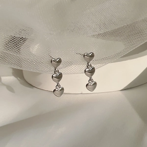 Three-tier silver heart dangle earrings on white lace backdrop with a polished finish