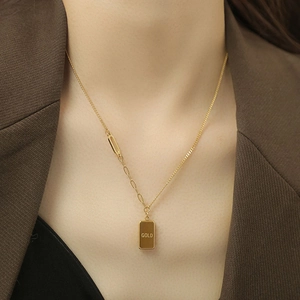 Detail of gold bar necklace with 'GOLD' engraving and asymmetrical chain on model