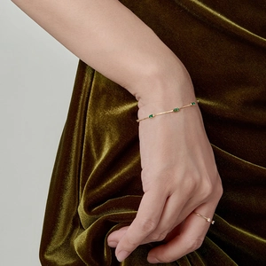 Elegant gold chain bracelet with three rectangular emerald stones on green velvet