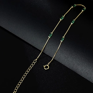 Elegant gold chain bracelet with six emerald-cut green gems on a textured black background