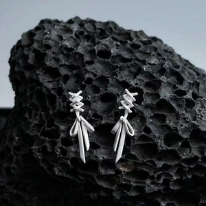 Matte S925 silver bow ribbon earrings displayed on a dark textured volcanic rock