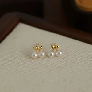 Exquisite cherry pearl stud earrings with gold bow design on a minimalist display