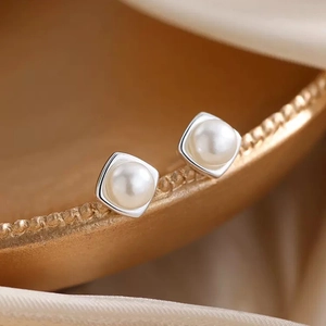 Eleganti orecchini a perno quadrati in argento con perla su sfondo di seta di lusso
