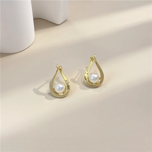 Elegant spiral water-drop gold earrings with white pearl detail on warm background